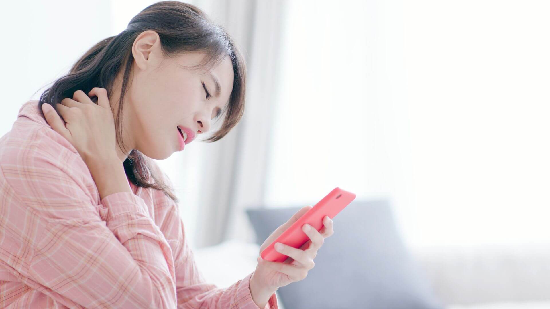 Woman experiencing neck pain while looking at smartphone, illustrating Text Neck Syndrome in the digital age.